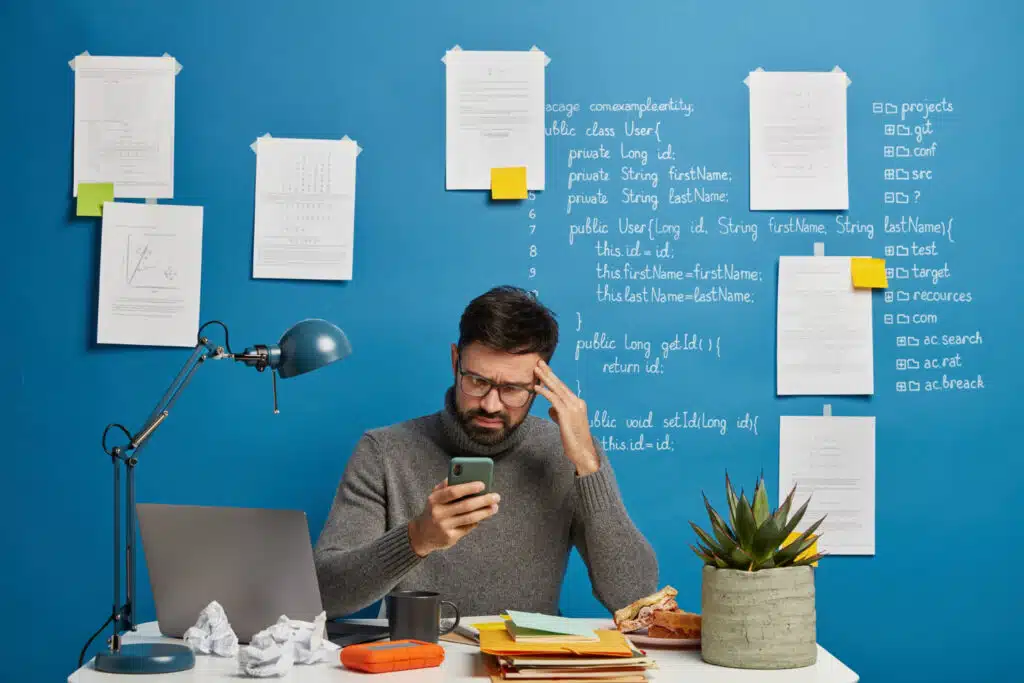 Homme au bureau distrait par son téléphone, illustrant la procrastination au travail