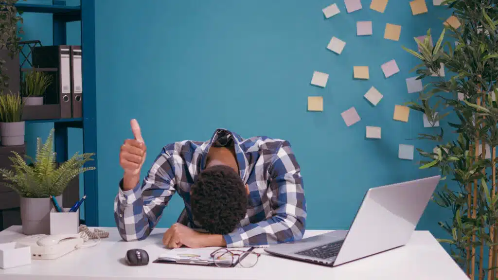 Homme fatigué au bureau levant le pouce malgré la procrastination et la surcharge de travail