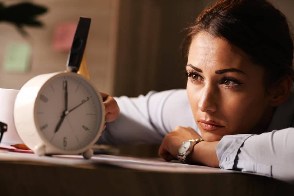 Femme fatiguée regardant un réveil symbolisant le temps perdu à procrastiner