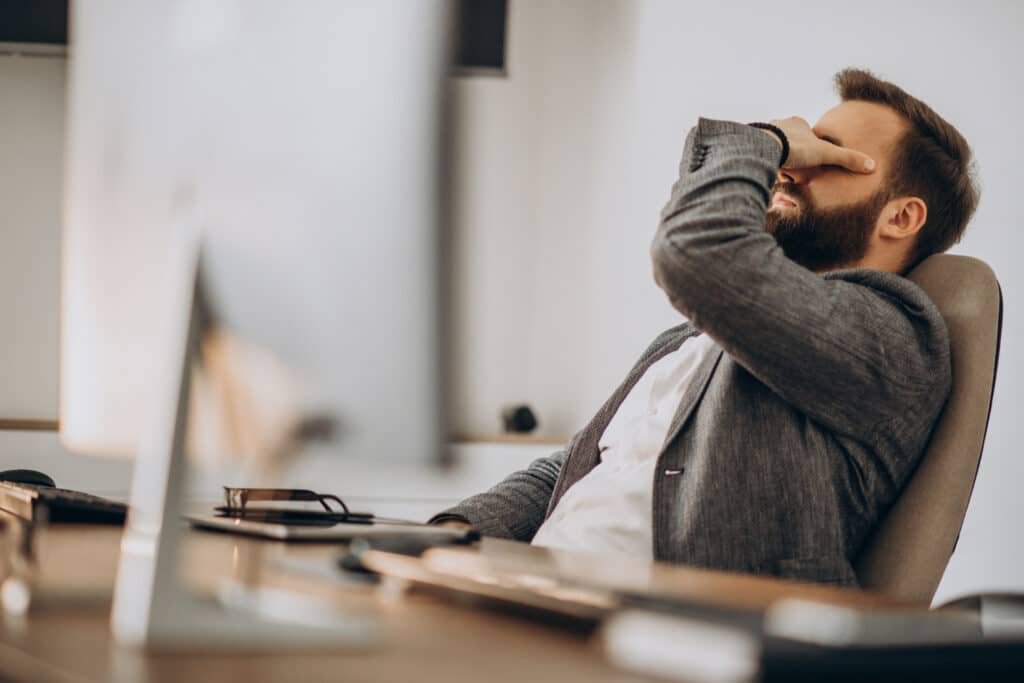Homme fatigué au bureau, la main sur le visage, illustrant les signes d’un Burn-out au travail.